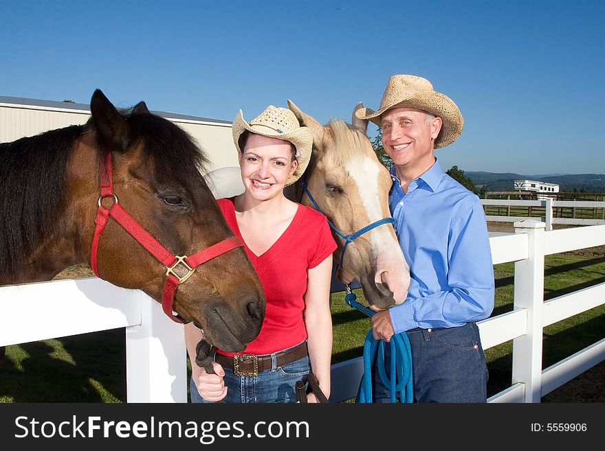 Smiling couple wearing cowboy hats stand next to their horses. Horizontally framed photograph. Smiling couple wearing cowboy hats stand next to their horses. Horizontally framed photograph.