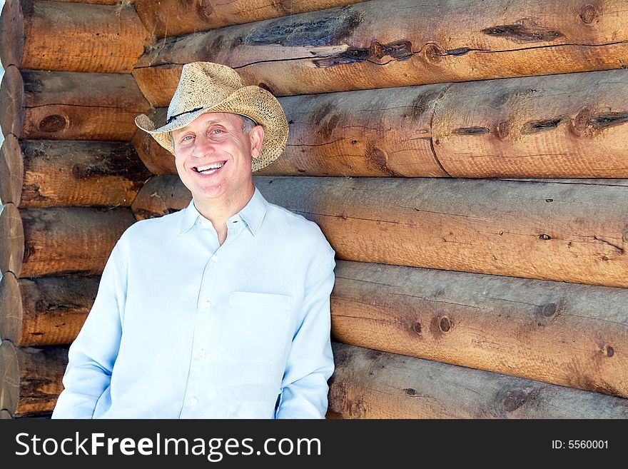 Laughing man in cowboy hat leaning against a log cabin. Horizontally framed photograph. Laughing man in cowboy hat leaning against a log cabin. Horizontally framed photograph