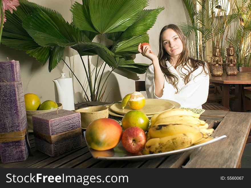 An attractive young girl holding an apple while outdoors, surrounded by fruits and plants. - horizontally framed. An attractive young girl holding an apple while outdoors, surrounded by fruits and plants. - horizontally framed