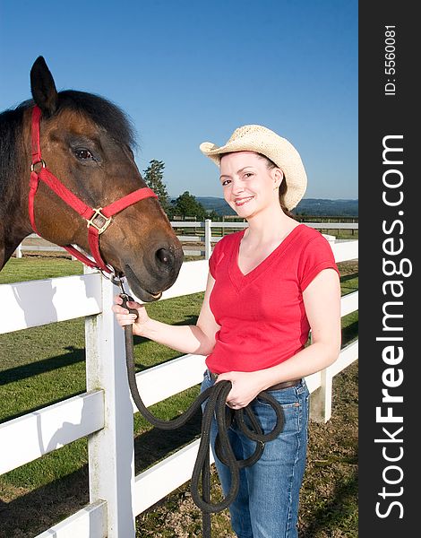 Smiling woman wearing a cowboy hat stands next to a brown horse. Vertically framed photograph. Smiling woman wearing a cowboy hat stands next to a brown horse. Vertically framed photograph.