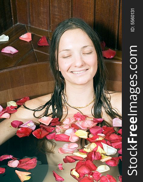 A Young girl smiling, while relaxing in a bathtub, with rose petals on the surface of the water. - vertically framed. A Young girl smiling, while relaxing in a bathtub, with rose petals on the surface of the water. - vertically framed