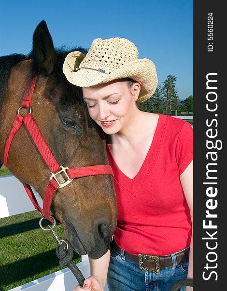 Smiling woman wearing a cowboy hat nuzzles next to a brown horse. Vertically framed photograph. Smiling woman wearing a cowboy hat nuzzles next to a brown horse. Vertically framed photograph.