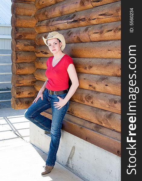 Woman in cowboy hat leaning against a log cabin with her leg propped up. Verictally framed photograph. Woman in cowboy hat leaning against a log cabin with her leg propped up. Verictally framed photograph