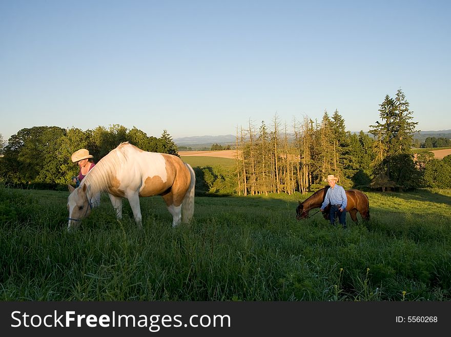 Two farmers walking their horses through grass on a hill. - Horizontally framed. Two farmers walking their horses through grass on a hill. - Horizontally framed