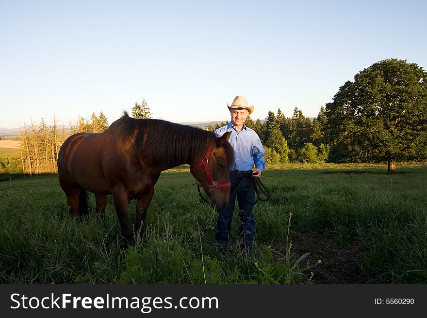 A male farmer smiles while his horse is beside him, in a grassy meadow. - horizontally framed. A male farmer smiles while his horse is beside him, in a grassy meadow. - horizontally framed