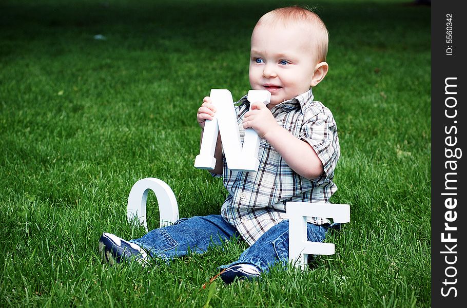 A baby seated in a field of grass holding a letter N. - horizontally framed. A baby seated in a field of grass holding a letter N. - horizontally framed