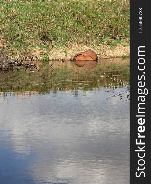 A rusting barrel sitting half submerged in a wetland pond. A rusting barrel sitting half submerged in a wetland pond