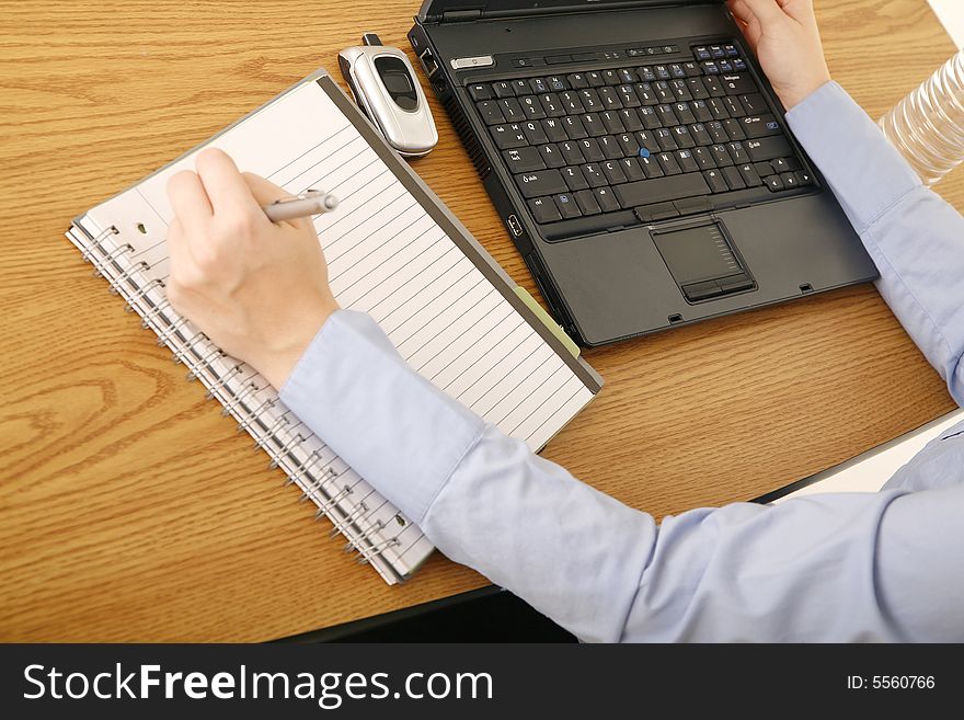 Shot of table with laptop and notepad with hand of woman in casual dress. Shot of table with laptop and notepad with hand of woman in casual dress