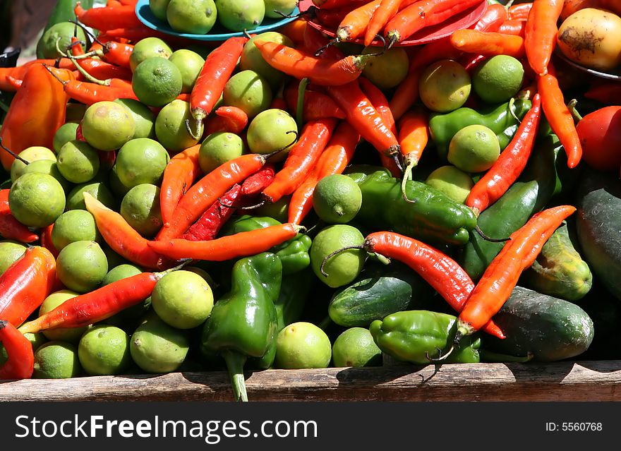 A cart full of fresh vegetables includng red peppers, green peppers, limes, and cucumbers. A cart full of fresh vegetables includng red peppers, green peppers, limes, and cucumbers