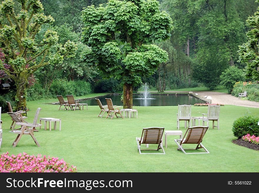 Garden with a small lake and wooden chairs waiting for people looking for a releax. Garden with a small lake and wooden chairs waiting for people looking for a releax