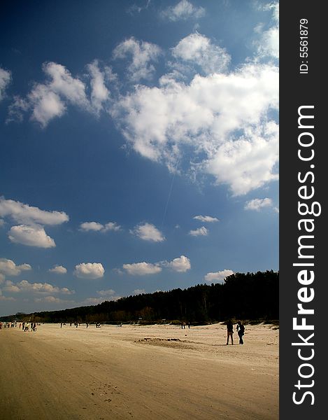 Beach of Riga Gulf with walking people under beautifull clouds in sunny spring day. Beach of Riga Gulf with walking people under beautifull clouds in sunny spring day