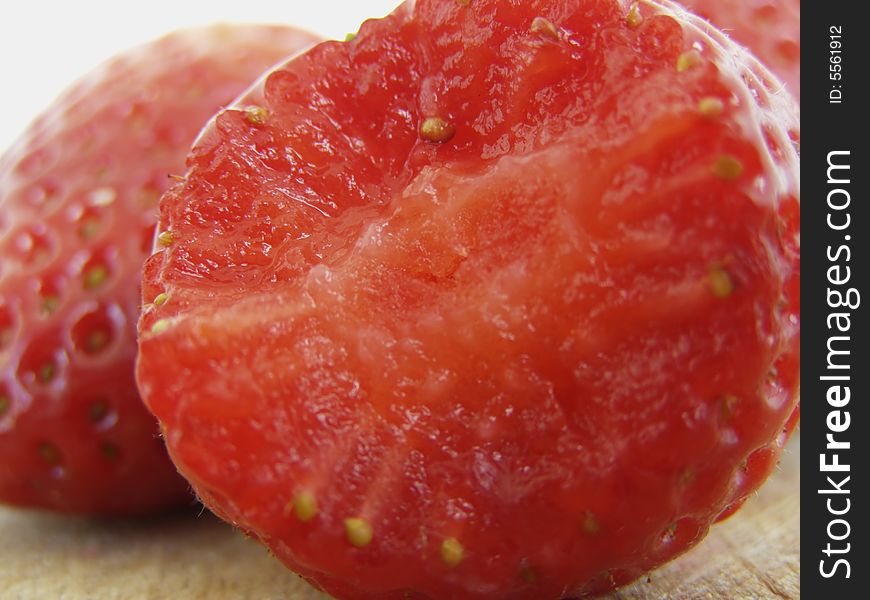 Strawberry macro with a bite, more strawberries in the background, on wooden kitchen board surface against white background, juicy details *RAW format available