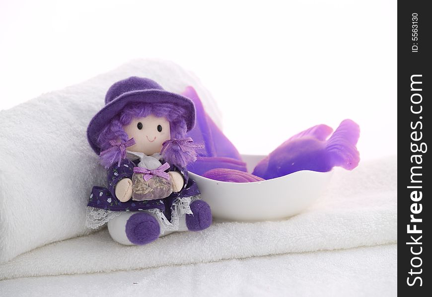Little rustic doll and lilac soaps laying at white towels, white background. Little rustic doll and lilac soaps laying at white towels, white background