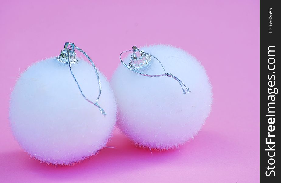 A shot of two white fluffy baubles against a pink background. A shot of two white fluffy baubles against a pink background