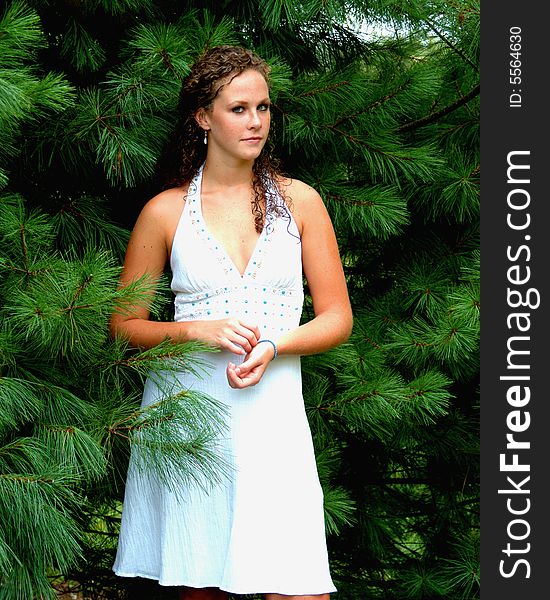 Young woman standing among pine trees in white dress with turquoise trim. Young woman standing among pine trees in white dress with turquoise trim