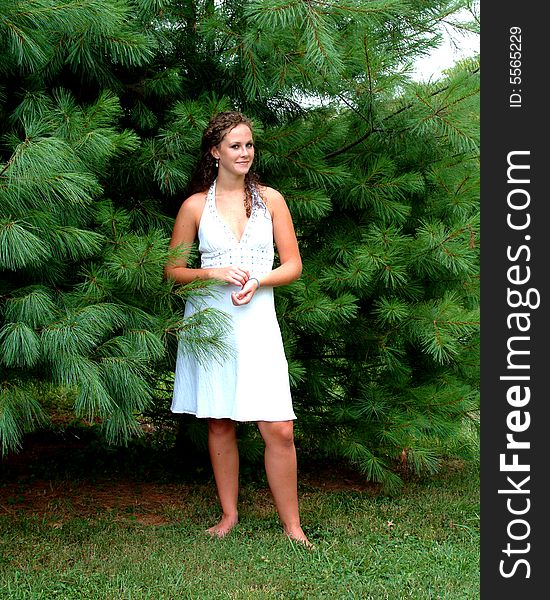 Young woman standing among pine trees in white dress with turquoise trim. Young woman standing among pine trees in white dress with turquoise trim