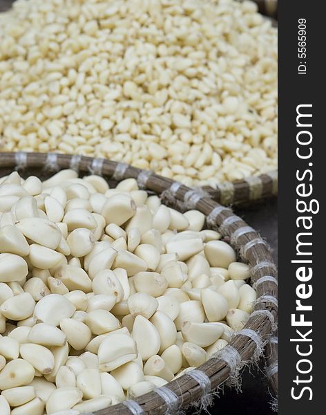 Baskets of peeled garlic at a market. In the foreground, large, in the backround and out of focus, small garlic.