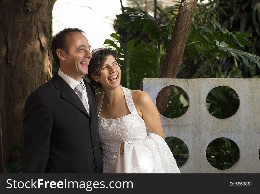 A newly married couple smile away from the camera, while still in their wedding clothes. A scenic area fills the background. - horizontally framed. A newly married couple smile away from the camera, while still in their wedding clothes. A scenic area fills the background. - horizontally framed