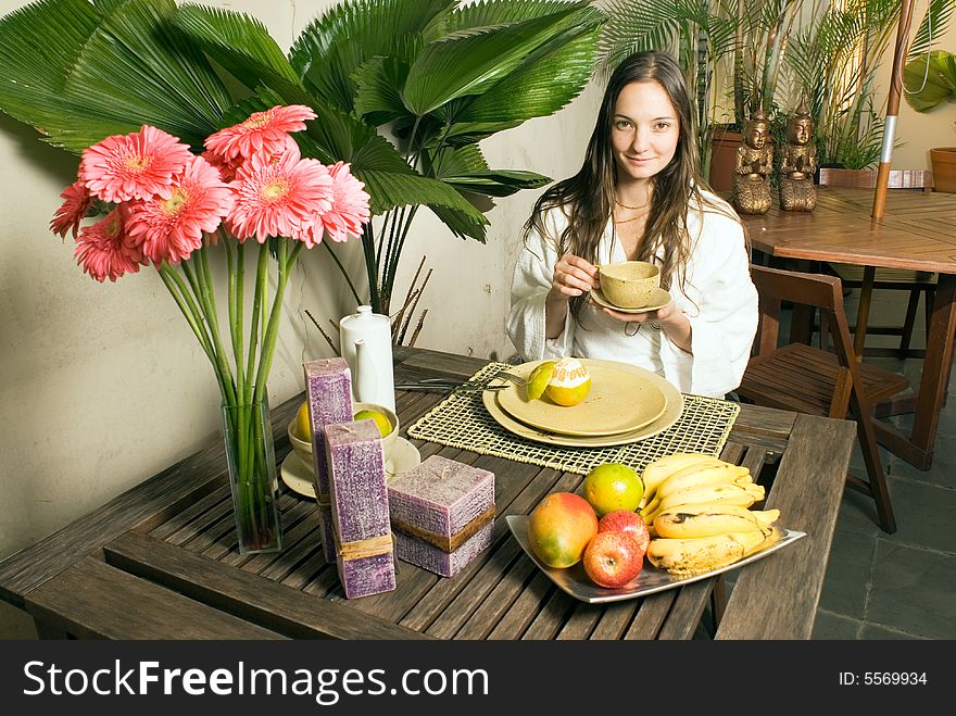 A young girl outside surrounded by plants, fruits, and flowers, holding a cup, smiling for the camera. - horizontally framed. A young girl outside surrounded by plants, fruits, and flowers, holding a cup, smiling for the camera. - horizontally framed