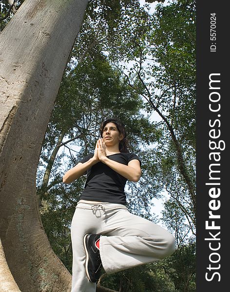 Young, attractive woman is standing next to a tree.   She appears to be performing yoga.  Vertically framed shot. Young, attractive woman is standing next to a tree.   She appears to be performing yoga.  Vertically framed shot