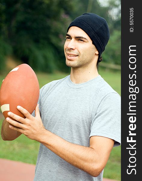 A man standing in a park, holding a football, ready to pass. - vertically framed. A man standing in a park, holding a football, ready to pass. - vertically framed
