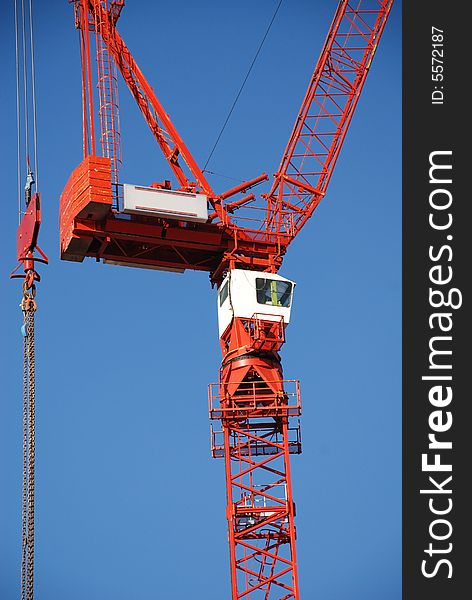 A red tower crane undertaking construction work, against a blue sky. A red tower crane undertaking construction work, against a blue sky