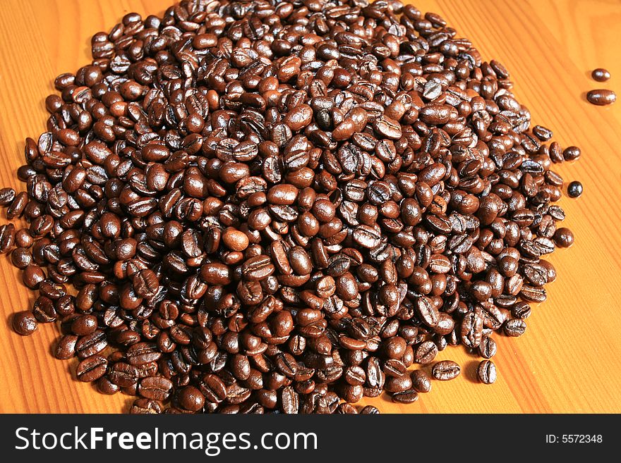 Grains of fragrant black coffee are poured a hill on a light wooden table