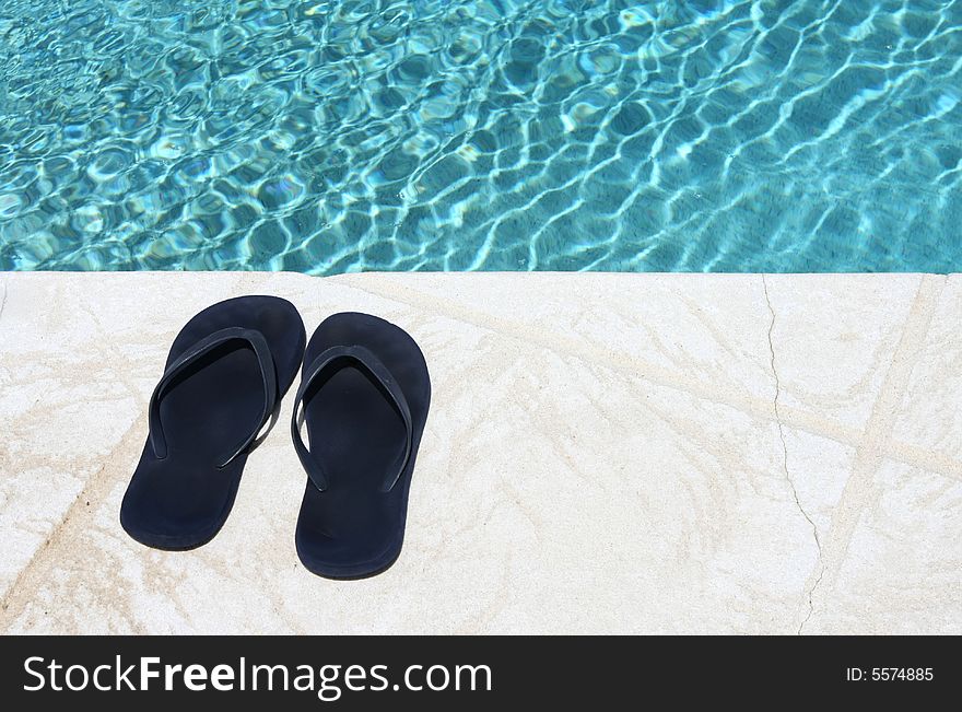 Two blue sandals next to pool water. Two blue sandals next to pool water