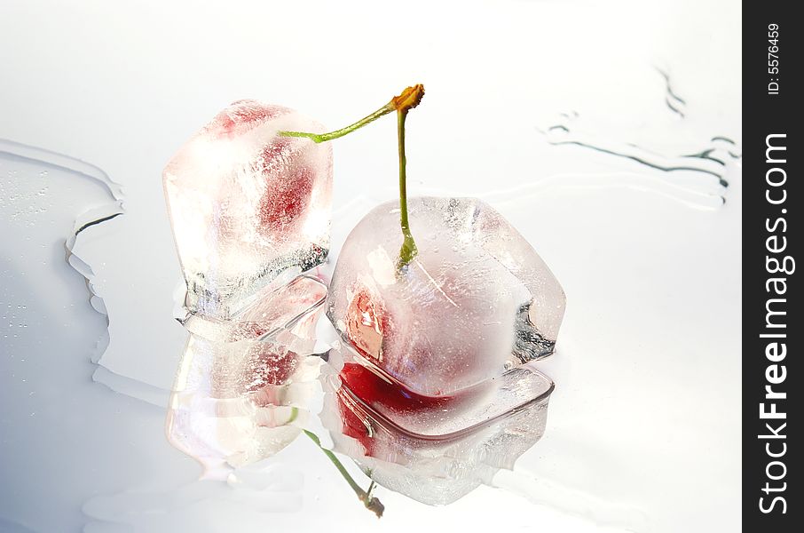 Two frozen cherries on white glass surface