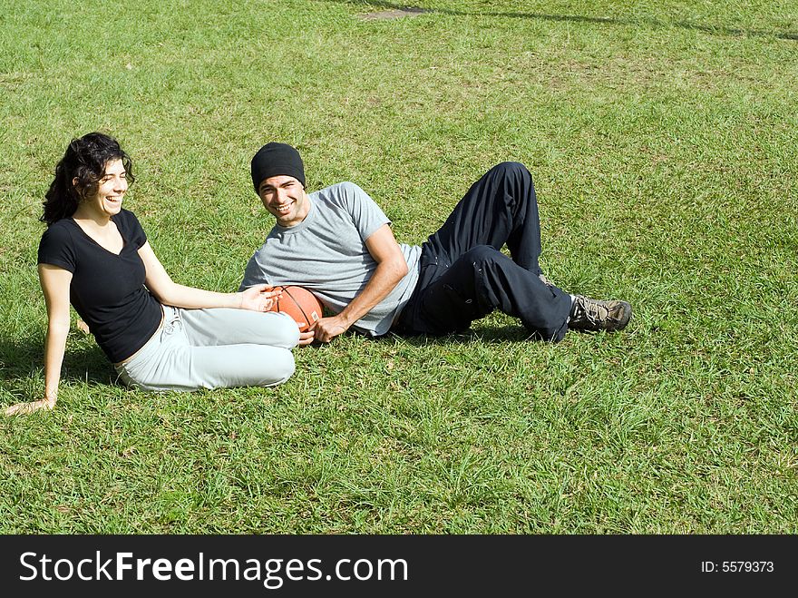 Young, attractive couple sitting and laughing together on grassy field.  Horizontally framed shot. Young, attractive couple sitting and laughing together on grassy field.  Horizontally framed shot.