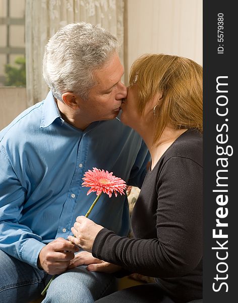 Romantic couple kissing on a couch, holding a bright flower. vertically framed shot. Romantic couple kissing on a couch, holding a bright flower. vertically framed shot.