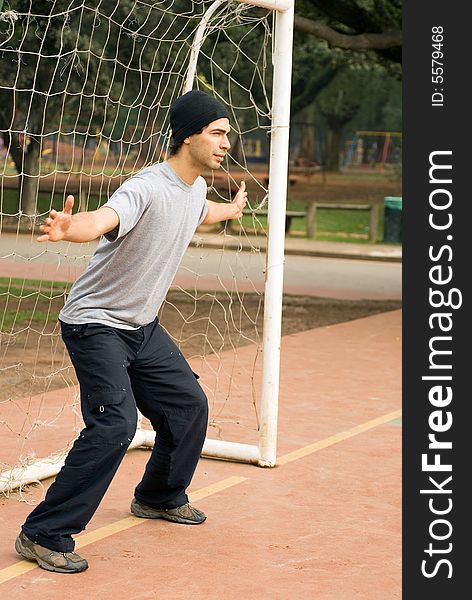 A man in a park, with his arms spread outwards, acts to be a goalie in front of a soccer goal. - vertically framed. A man in a park, with his arms spread outwards, acts to be a goalie in front of a soccer goal. - vertically framed