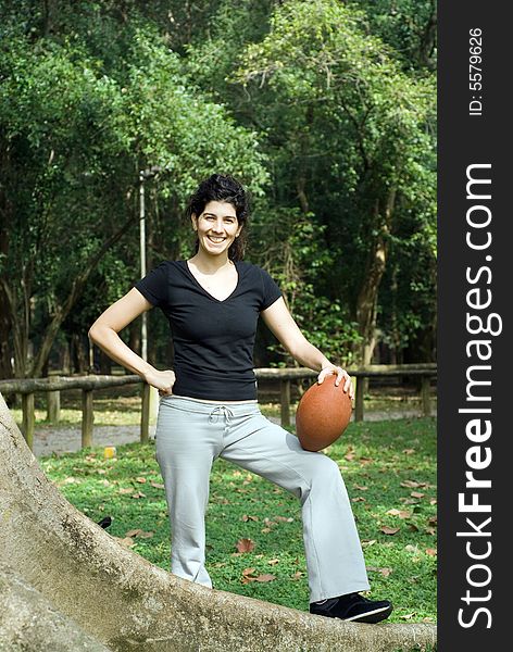 Young, attractive woman is posing next to a tree.  She is smiling and holding a football.   Vertically framed shot. Young, attractive woman is posing next to a tree.  She is smiling and holding a football.   Vertically framed shot