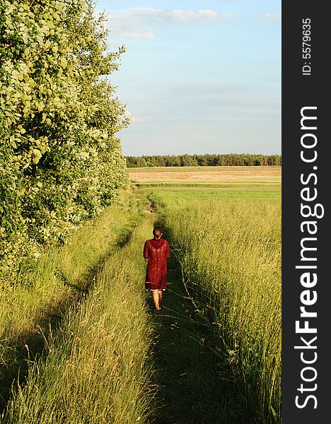 The girl having an evening walk along the field in Lithuania.