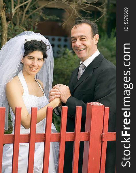 A couple, newly married, smile for the camera while holding hands behind a red gate. - vertically framed. A couple, newly married, smile for the camera while holding hands behind a red gate. - vertically framed