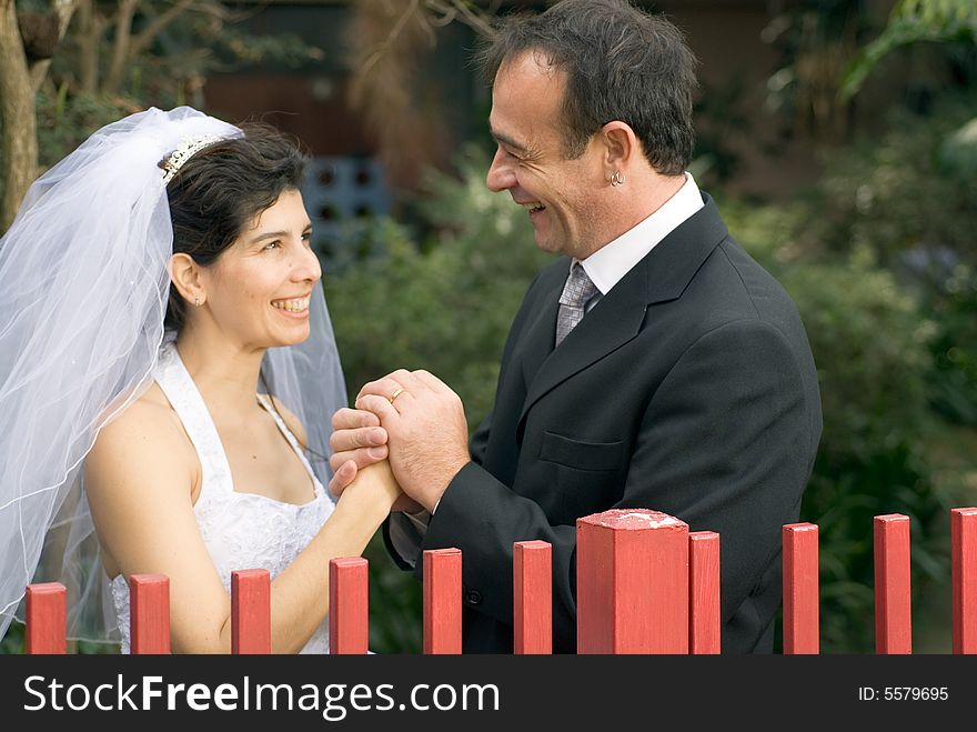 A newly married couple, stare at each other behind a red gate, holding hands and smiling. - horizontally framed. A newly married couple, stare at each other behind a red gate, holding hands and smiling. - horizontally framed