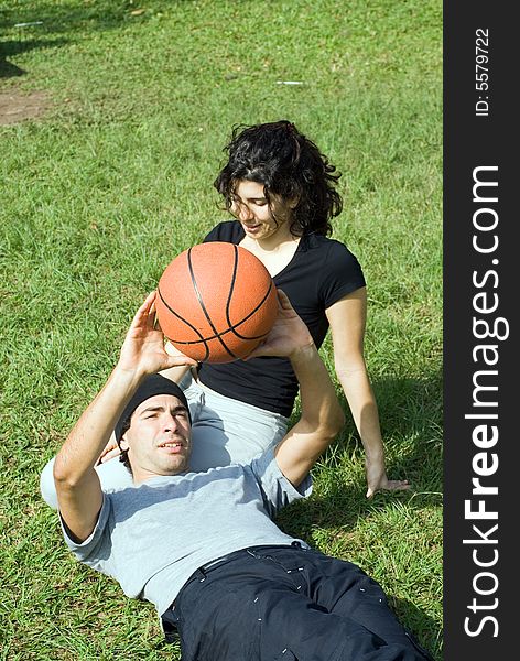 Young, attractive couple sitting together on a grassy field.  The man is laying across the woman's lap and holding up a basketball.  Vertically framed shot. Young, attractive couple sitting together on a grassy field.  The man is laying across the woman's lap and holding up a basketball.  Vertically framed shot.