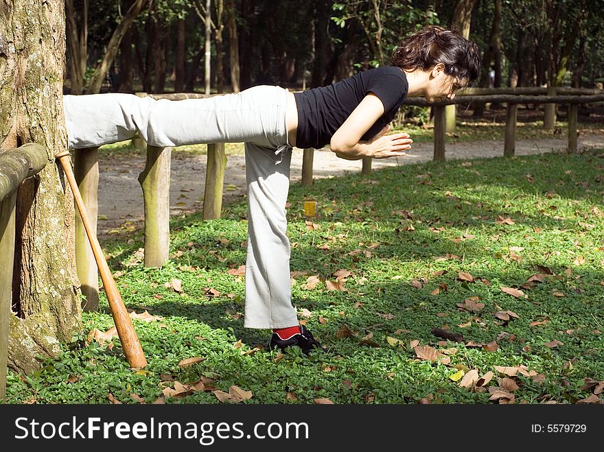 A woman is standing in a yoga pose next to a tree.  She is stretching her muscles.  A baseball bat is leaning against the tree.  Horizontally framed photo. A woman is standing in a yoga pose next to a tree.  She is stretching her muscles.  A baseball bat is leaning against the tree.  Horizontally framed photo.