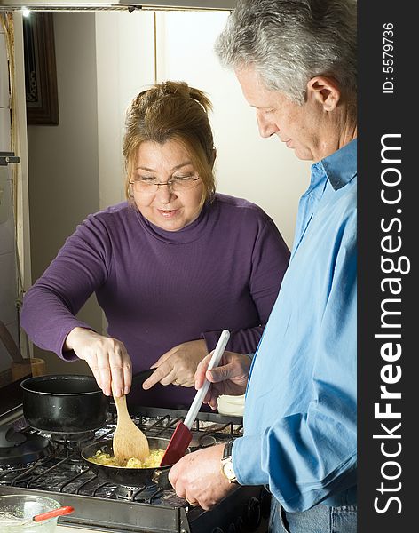 A couple, standing over the stove, creating scrambled eggs in a frying pan. - vertically framed. A couple, standing over the stove, creating scrambled eggs in a frying pan. - vertically framed