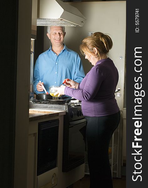 A couple preparing a meal on a stove, smiling. - vertically framed. A couple preparing a meal on a stove, smiling. - vertically framed