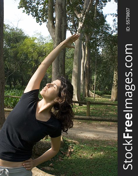 A woman is standing in the park. She is stretching her arms upward. Vertically framed photo. A woman is standing in the park. She is stretching her arms upward. Vertically framed photo.