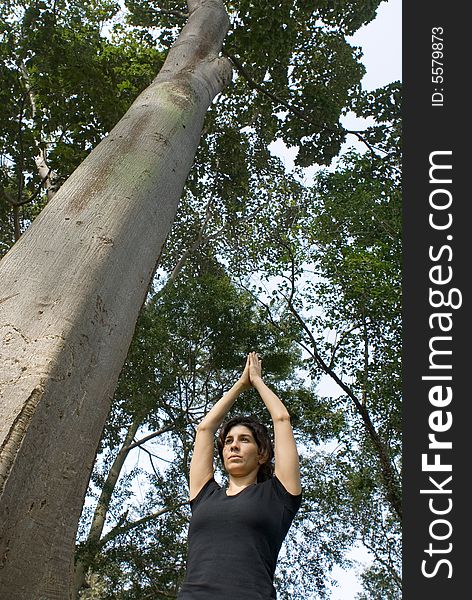 Young, attractive woman is standing next to a tree.   She appears to be performing yoga.  Vertically framed shot. Young, attractive woman is standing next to a tree.   She appears to be performing yoga.  Vertically framed shot