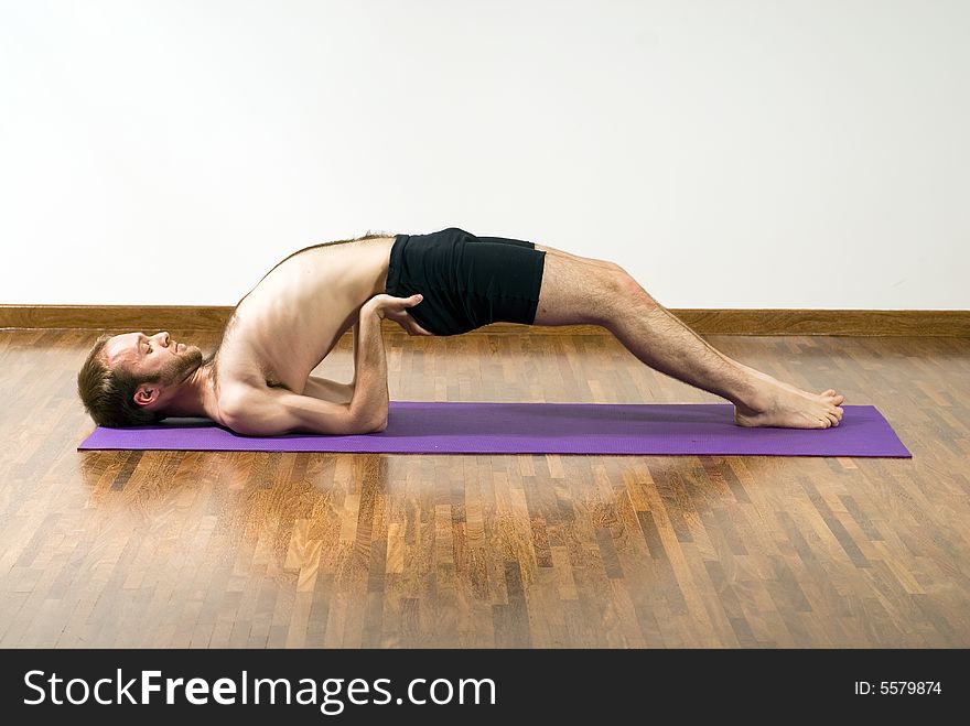 A man, on a purple foam mat, arching his back, stretching. - horizontally framed. A man, on a purple foam mat, arching his back, stretching. - horizontally framed