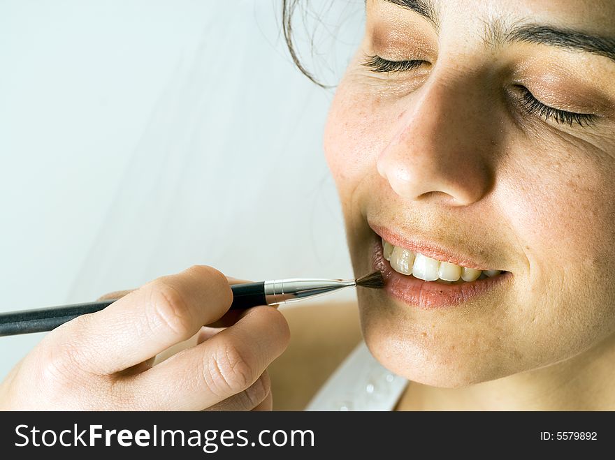 A soon-to-be wife puts on lipstick with a brush, smiling, with her eyes closed. - horizontally framed. A soon-to-be wife puts on lipstick with a brush, smiling, with her eyes closed. - horizontally framed