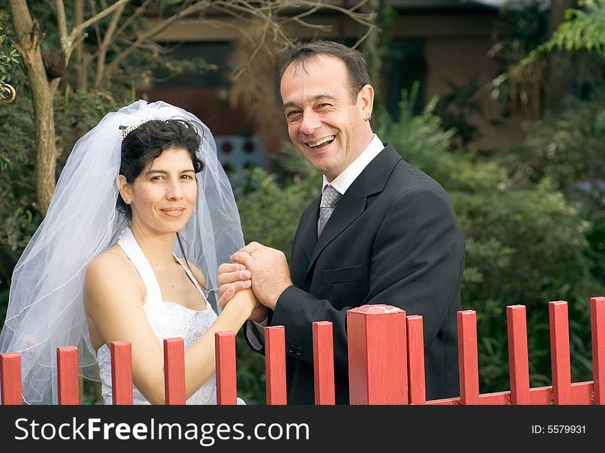 A newly married couple, behind a red gate, hold hands and smile. - horizontally framed. A newly married couple, behind a red gate, hold hands and smile. - horizontally framed