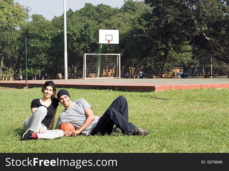 Attractive young couple smiling and laying together on the grass in a a park.  The man is holding a basketball.  Horizontally framed shot. Attractive young couple smiling and laying together on the grass in a a park.  The man is holding a basketball.  Horizontally framed shot.