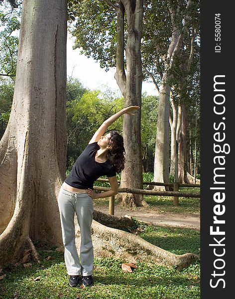 A woman is standing in the park.  She is stretching her arms upward.  Vertically framed photo. A woman is standing in the park.  She is stretching her arms upward.  Vertically framed photo.