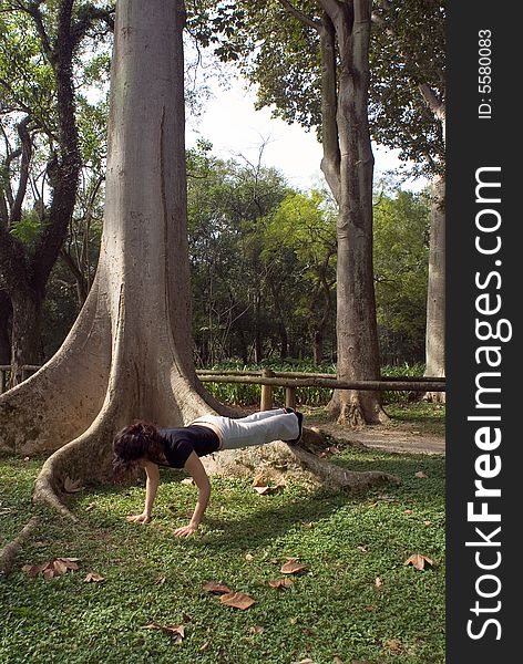 Young, attractive woman is performing a push-up next to a tree.   Vertically framed shot. Young, attractive woman is performing a push-up next to a tree.   Vertically framed shot