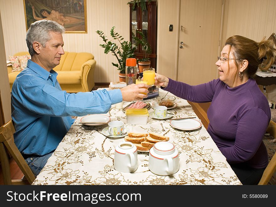 A couple toasting glasses of orange juice while at the table, preparing to eat. - horizontally framed. A couple toasting glasses of orange juice while at the table, preparing to eat. - horizontally framed