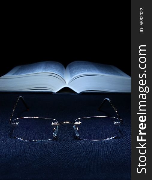 Glasses on the foreground and open book in the background. Glasses on the foreground and open book in the background